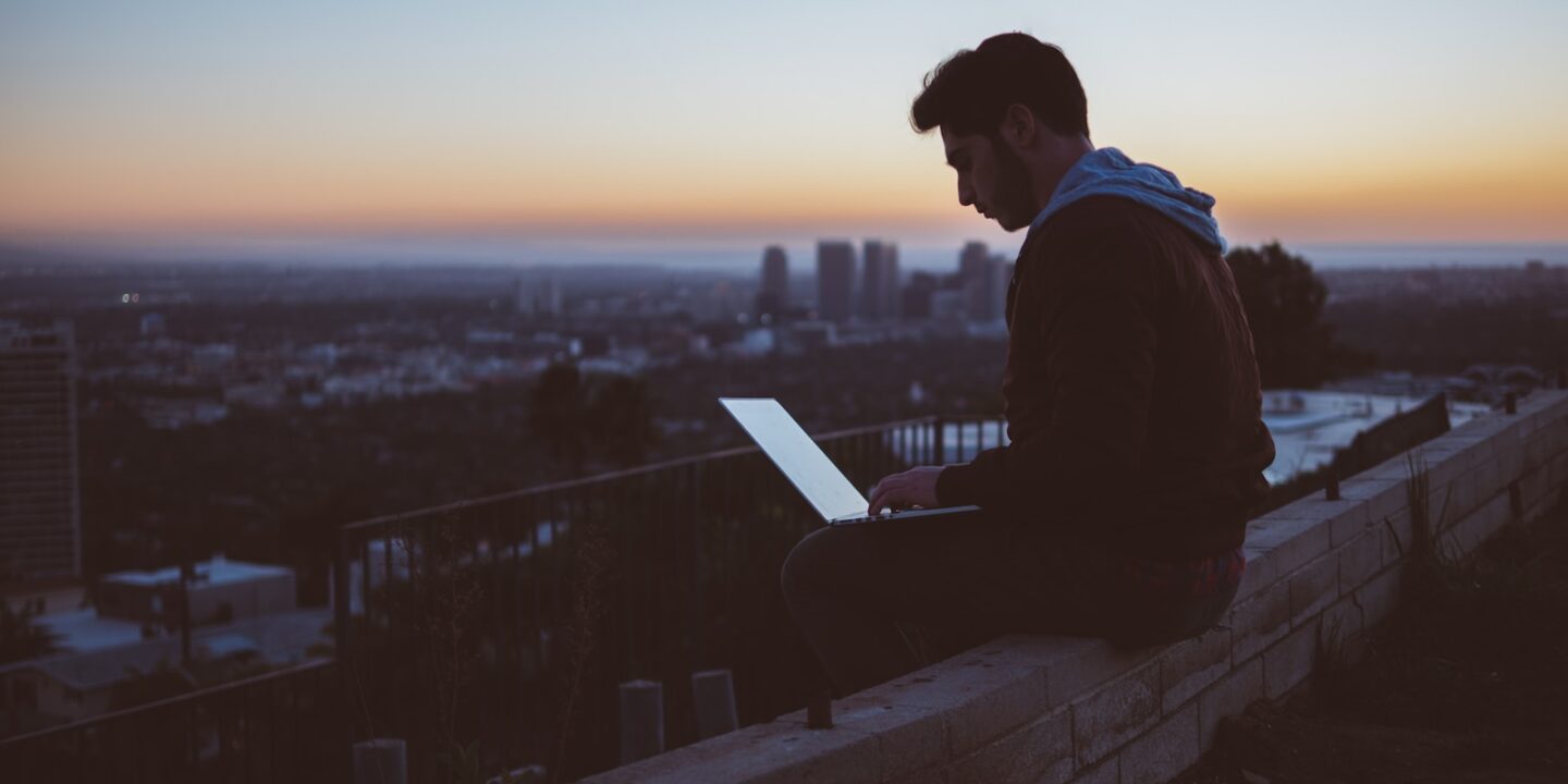 man sitting on concrete brick with opened laptop on his lap