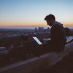 man sitting on concrete brick with opened laptop on his lap