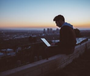 man sitting on concrete brick with opened laptop on his lap