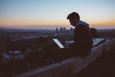 man sitting on concrete brick with opened laptop on his lap